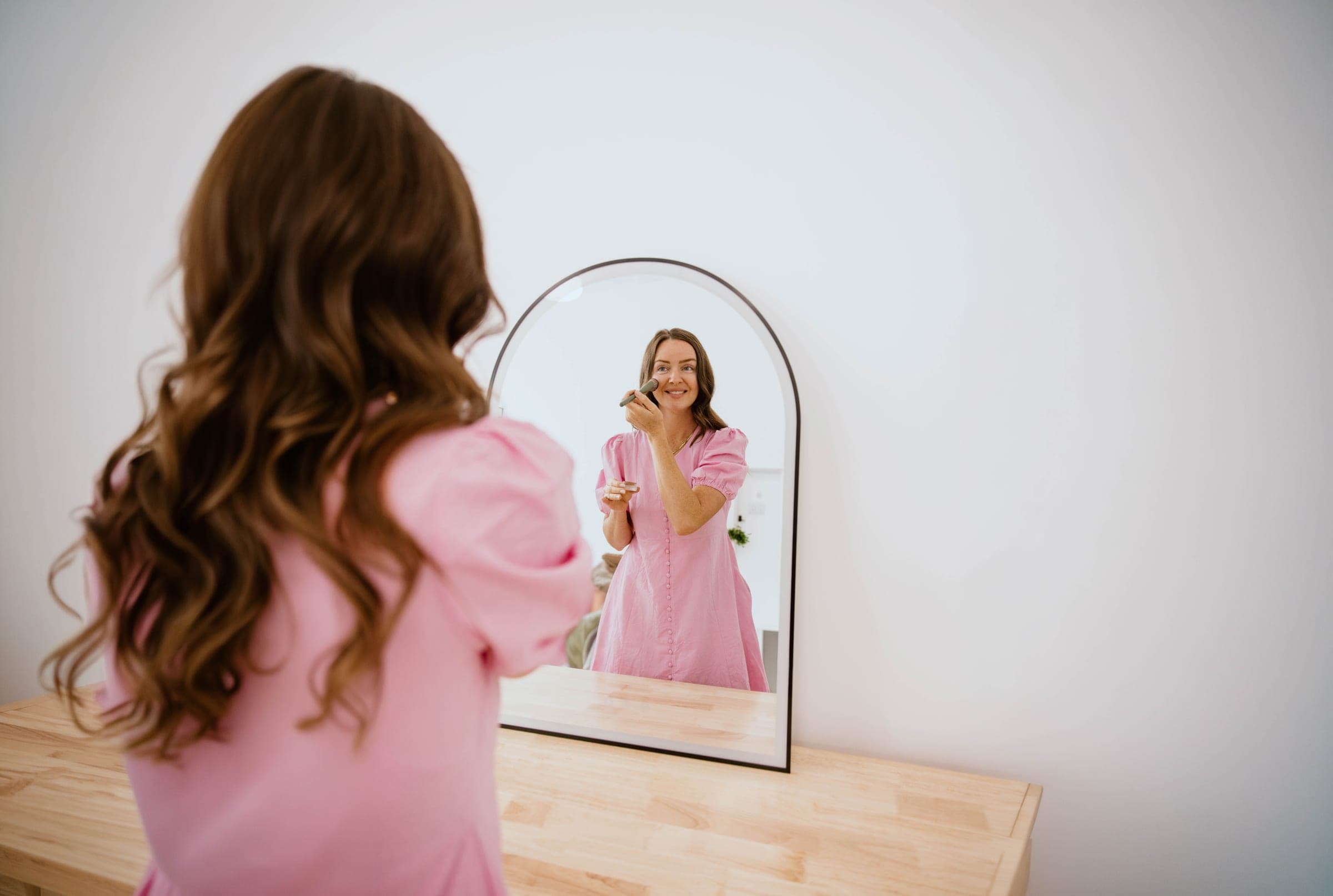 Woman in a pink cotton dress looking into a mirror