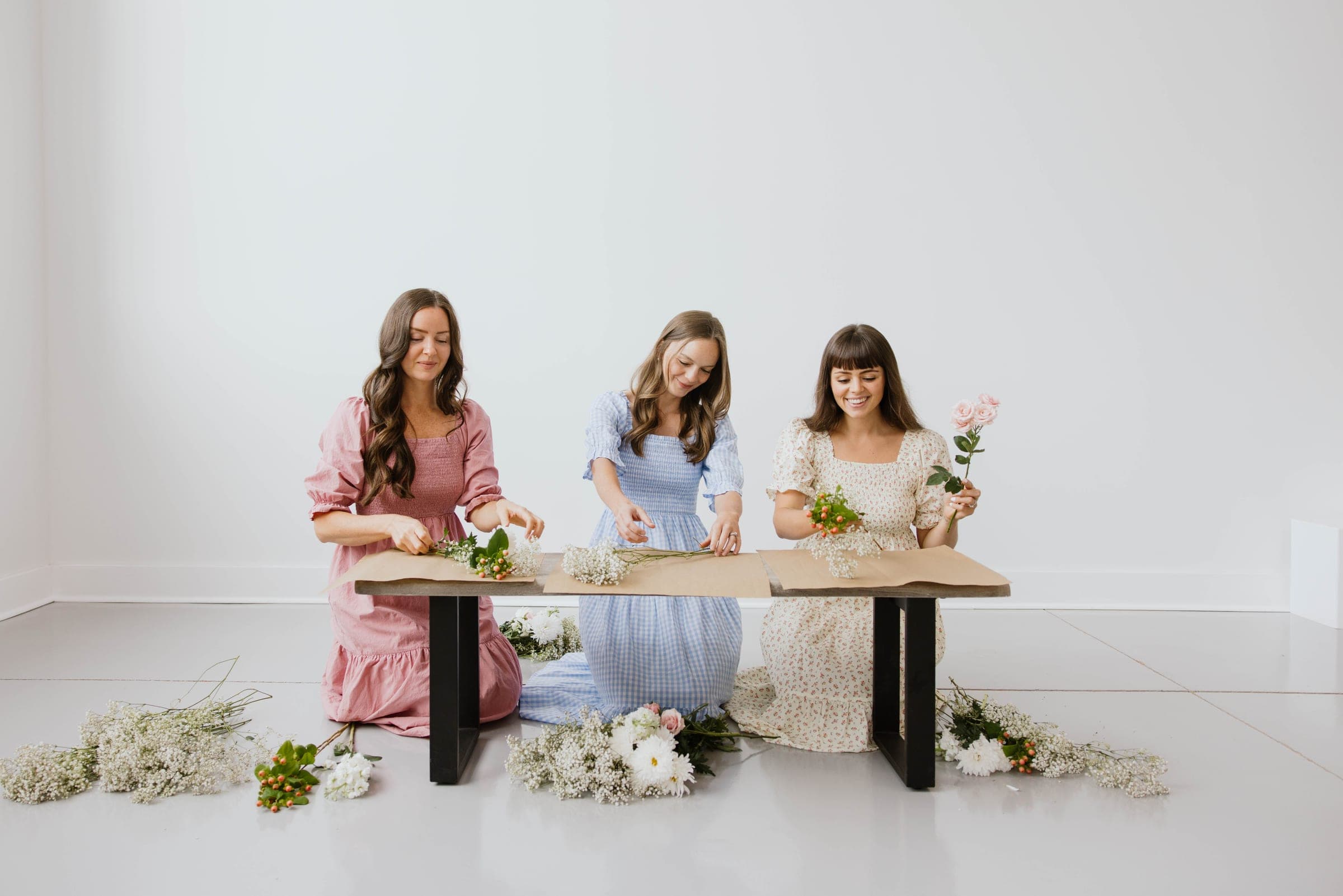 Three women in cotton dresses arranging flowers at a table