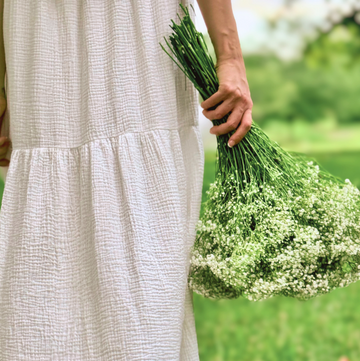 Person in a white dress holding a bouquet of flowers in a natural setting